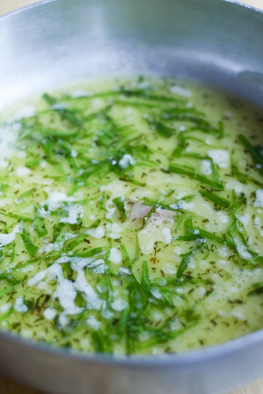 A metal pan with butter sauce and fresh tarragon