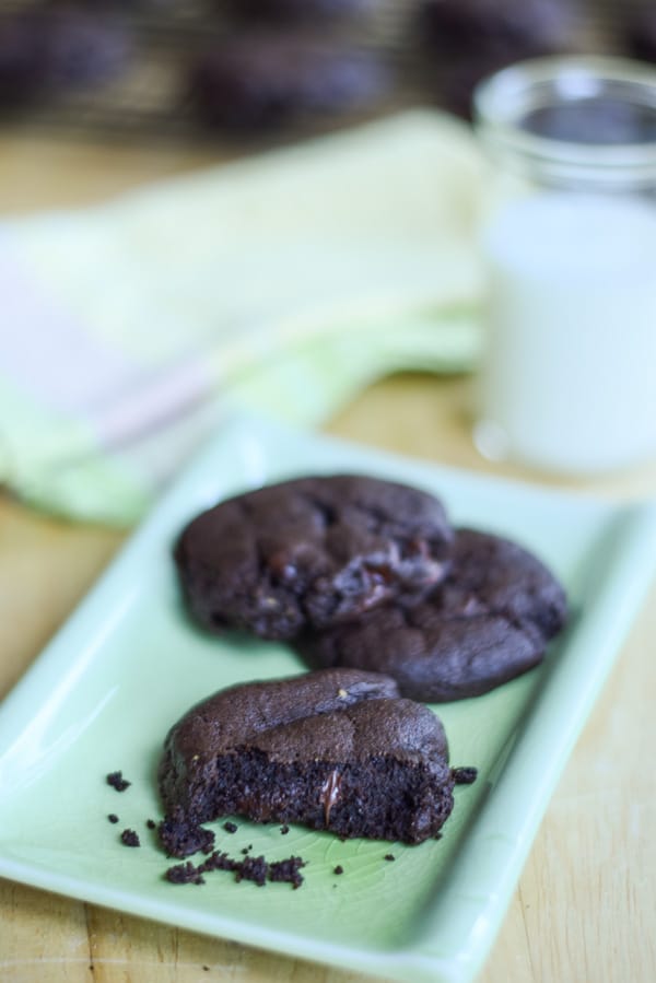 Dark chocolate cookies on a green rectangle plate with milk and more cookies in the background