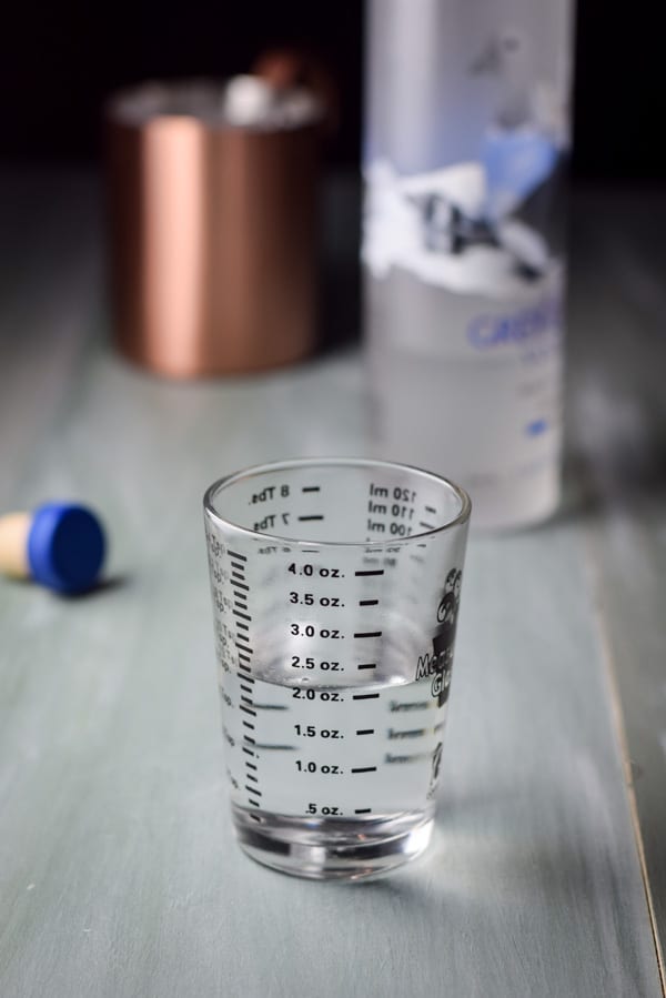 2 ounces of vodka poured out with the bottle and mug in the background