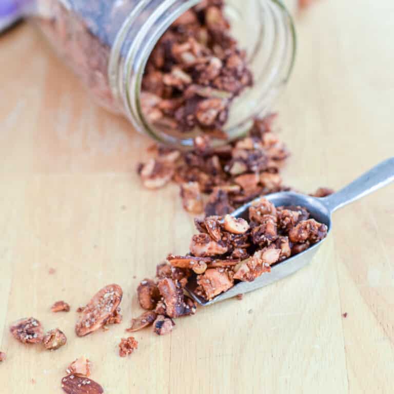 A scoop with granola spilling off it with a jar on it's side behind it