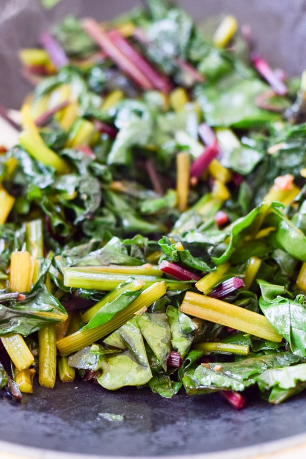 A wok with greens being sautéed in a wok