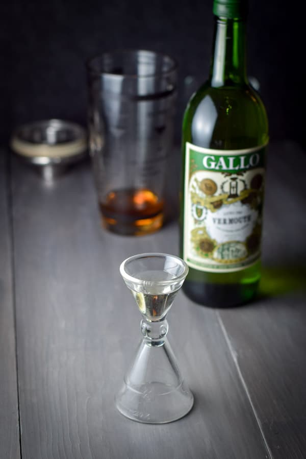 Dry vermouth measured out with the bottle and cocktail shaker in the background