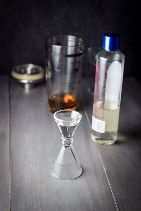 Simple syrup measured out with the bottle, shaker and glass in the background