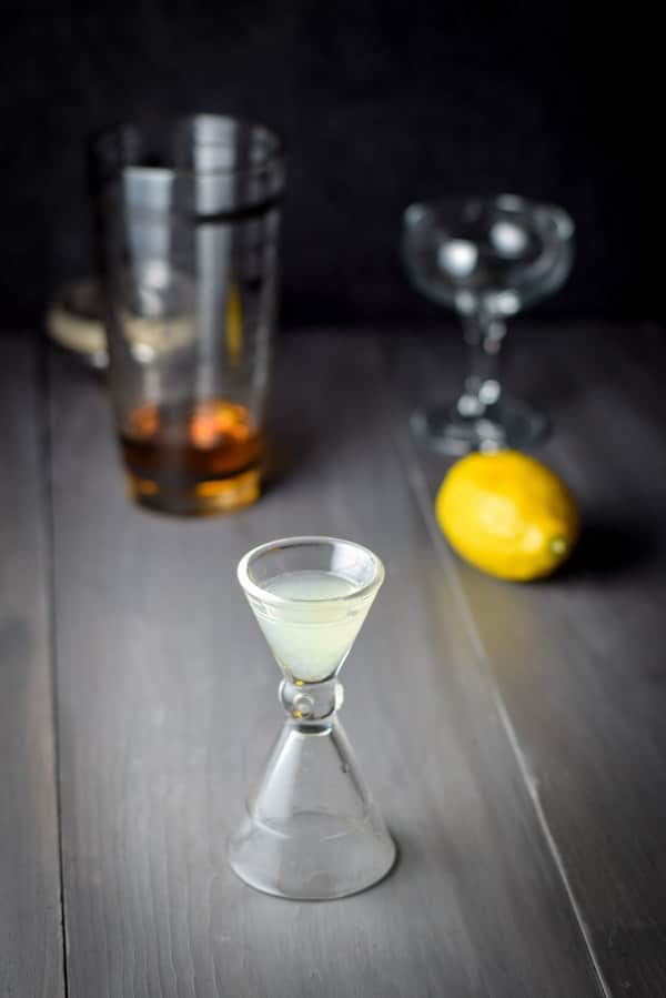 Lemon juice measured out with the fruit, glass and cocktail shaker in the background
