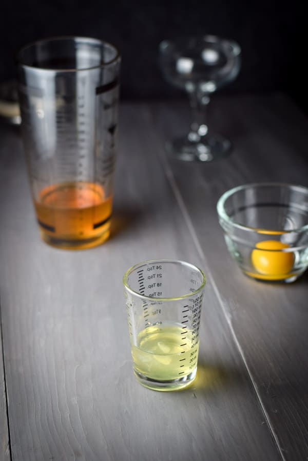 Egg white in a measuring glass with a cocktail shaker and glass in the background