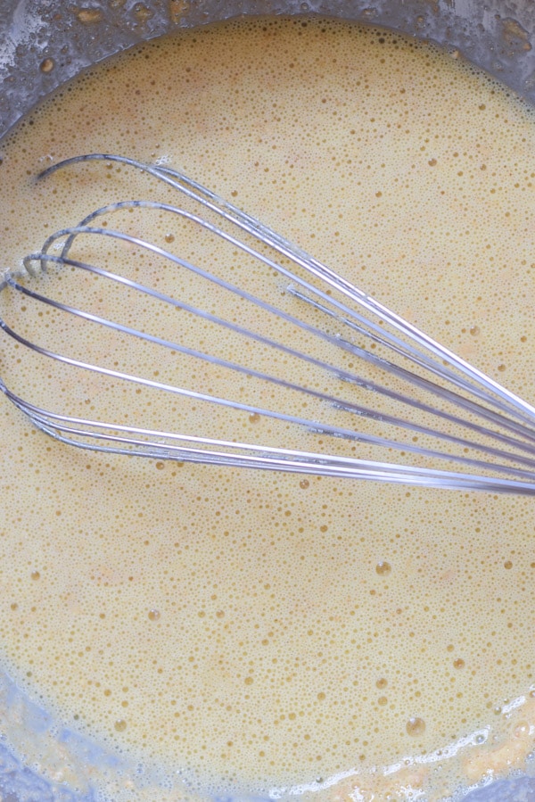 A metal bowl with eggs and milk whisked together