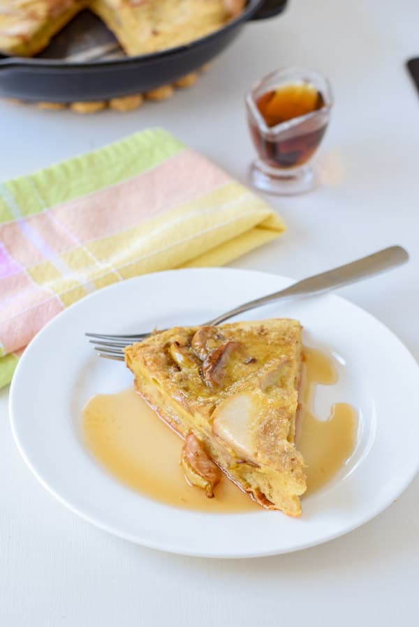 A white plate with a slice of the pancake on it with maple syrup on it and the little pourer filled with the syrup