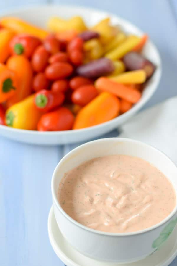 The dipping sauce in a white bowl with vegetables in the background