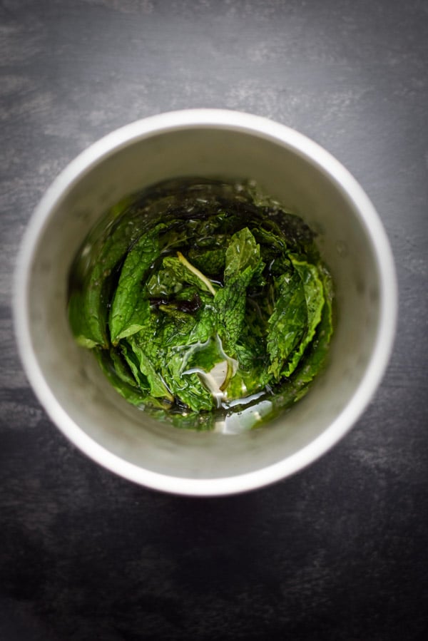 Overhead view of muddled mint and simple syrup in a metal cup