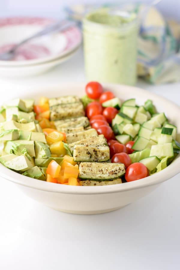 The avocado added to the salad with some dressing in the background