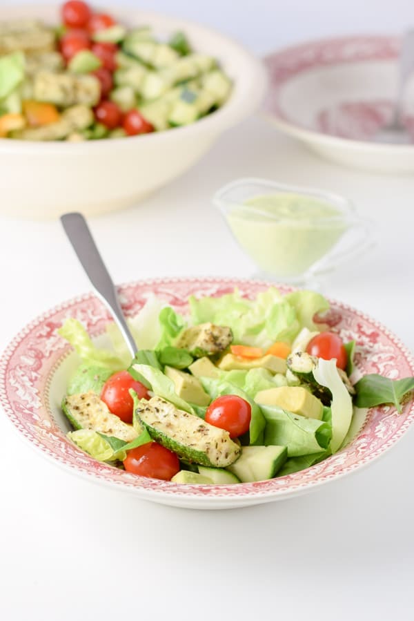 The salad served in a pink bowl and the dressing in a little container
