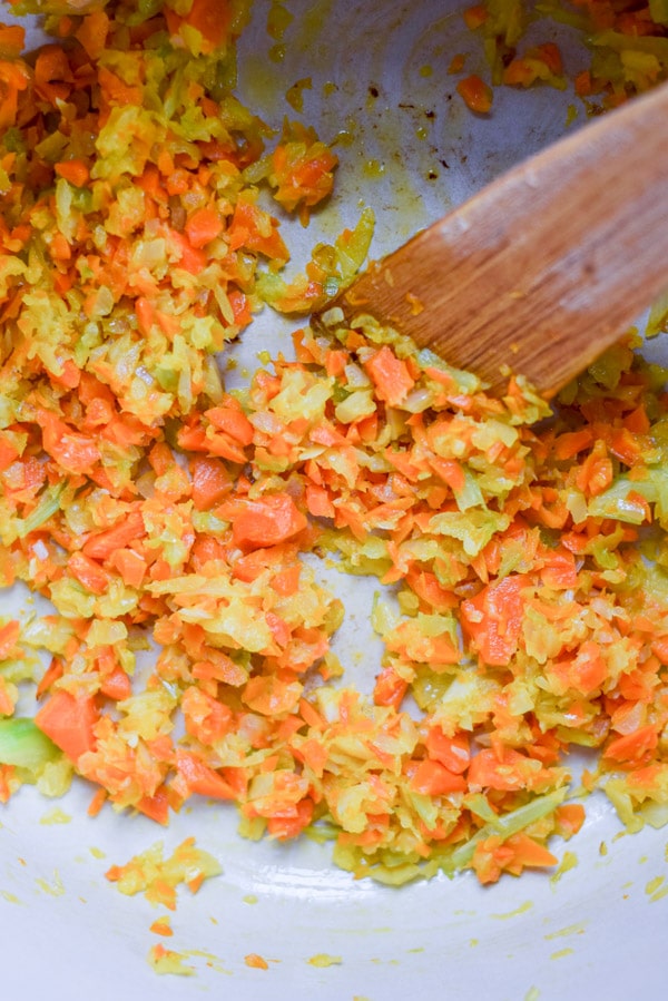 Overhead view of onion, carrot and celery sautéed in a pan with a wooden spatula in it