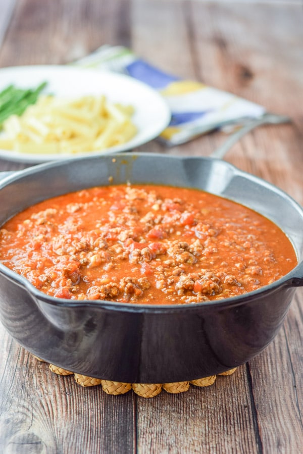 Gravy in a cast iron pan with a white plate with pasta in the background