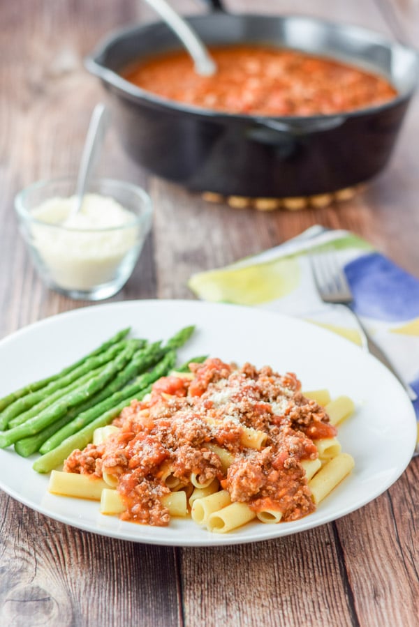 Parmesan cheese sprinkled on the gravy covered pasta with the pan of red sauce in the background