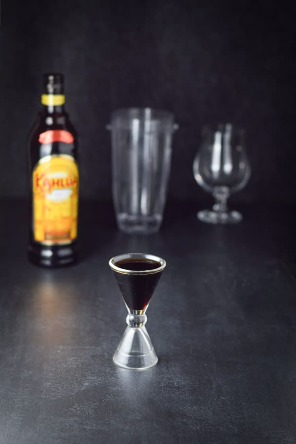 Kahlúa measured out with the bottle, container and glass in the background