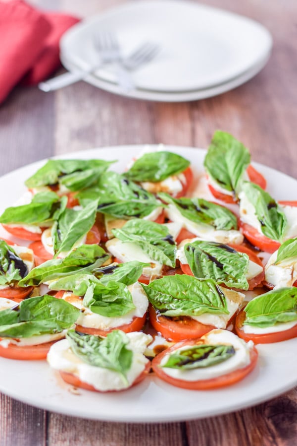 White plate with the tomato, basil and cheese salad with two other places in the background