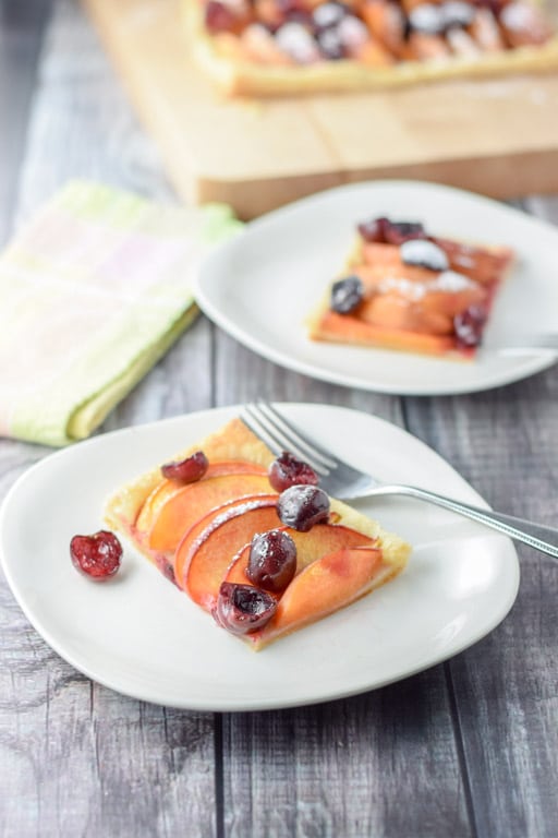 Two square plates with the fruit tart on them with a board with the rest of the tart in the background