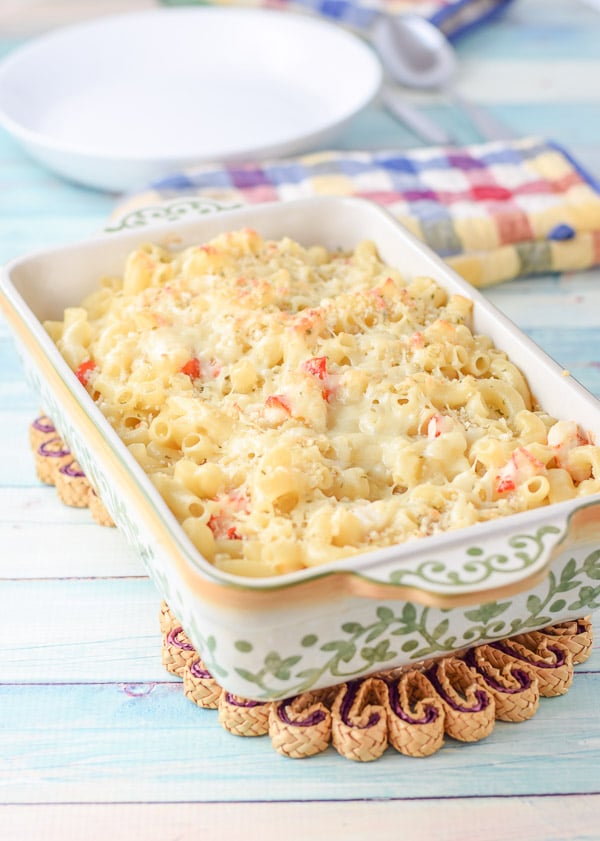 A baking dish with cheesy lobster pasta with a white bowl in the background