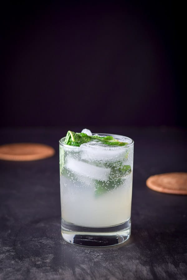 A ginger and grapefruit mojito on a black table with coasters in the background