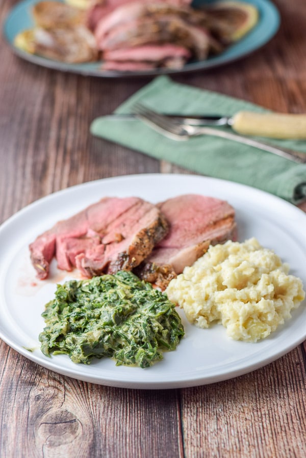 A white plate with spinach, mashed celery and lamb