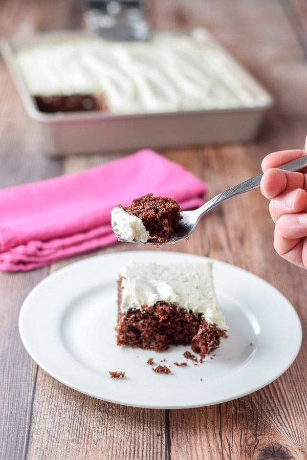 Forkful of chocolate cake over a plate with a pink napkin in the background