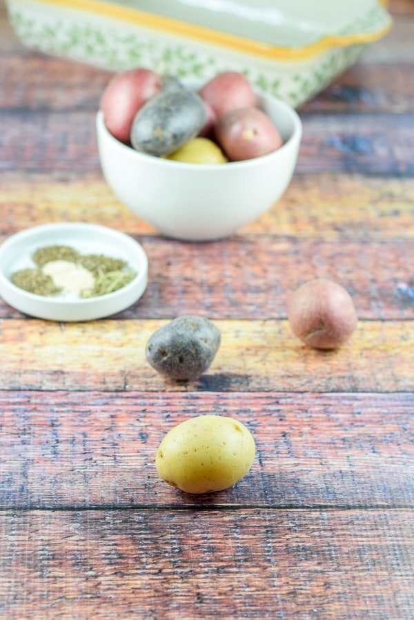 colorful potatoes on the table with more in a white bowl and a little white dish with herbs