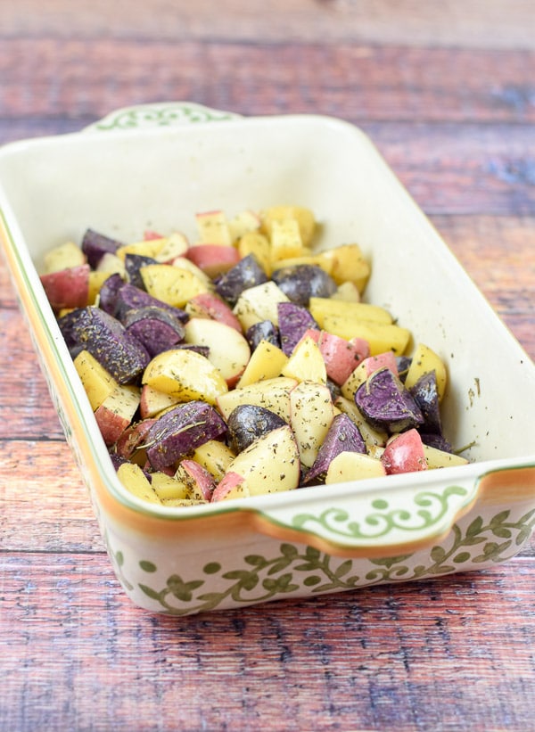 Raw potatoes in the baking dish with the herbs and spices on it