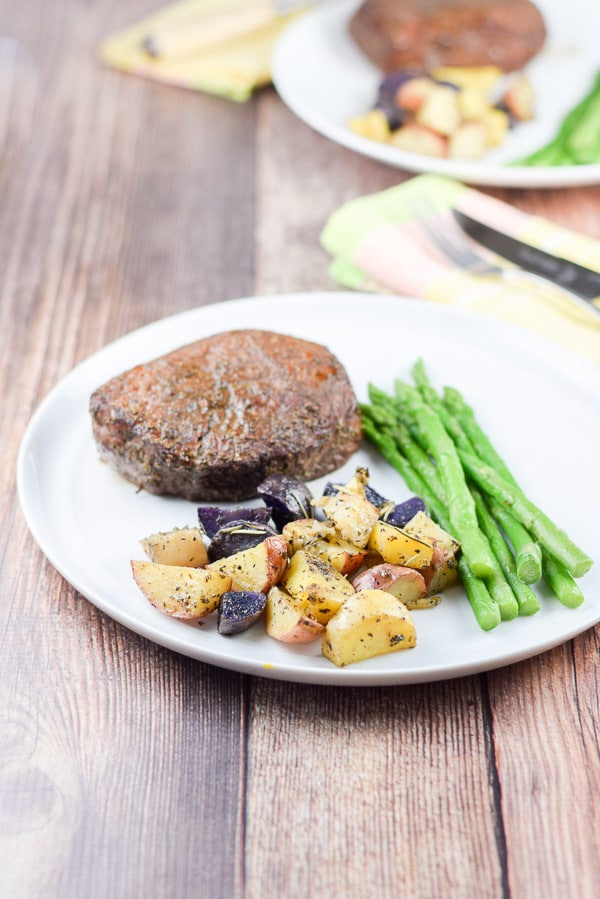 Potatoes and herbs on a white plate with asparagus and a steak