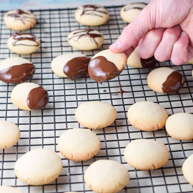 A hand holding a cookie that was dipped in chocolate held over a wire rack with more cookies on it