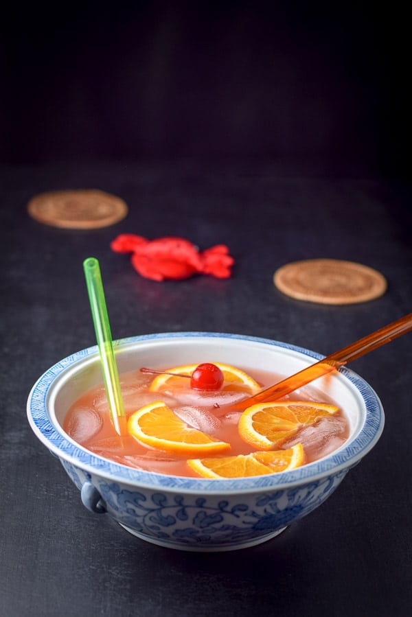blue bowl filled with the cocktail with oranges, cherries and straws in it