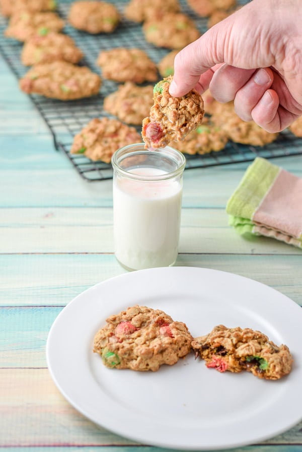 A male hand holding a cookie above a glass of milk