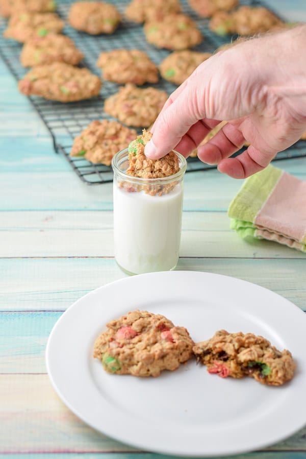 A male hand dunking a cookie in the milk with the plate in the foreground and the rack of cookies in the back