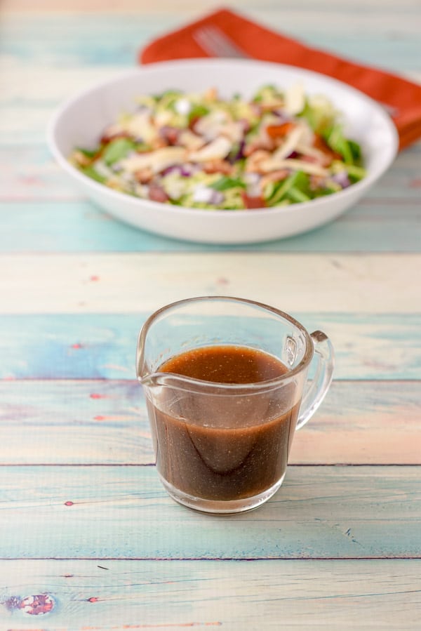 Dressing in a small glass pitcher with the salad behind it