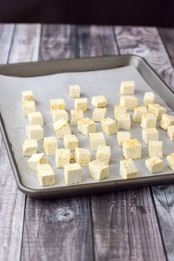 Curry coated tofu cubes on a parchment paper lined jelly roll pan