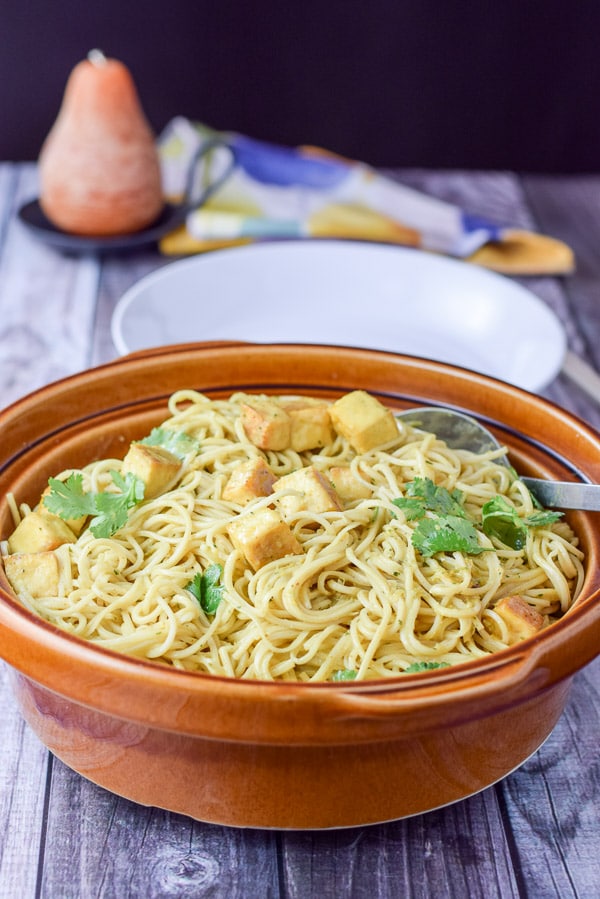 Noodles and tofu in a brown bowl with a deep dish and candle in the background