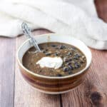 A brown bowl of bean soup with a dollop of sour cream in it as well as a spoon