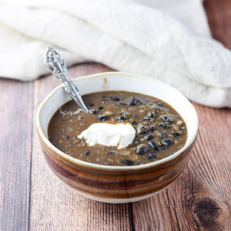 A brown bowl of bean soup with a dollop of sour cream in it as well as a spoon
