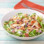 A deep white bowl with the salad in it and a napkin and fork in the background - square