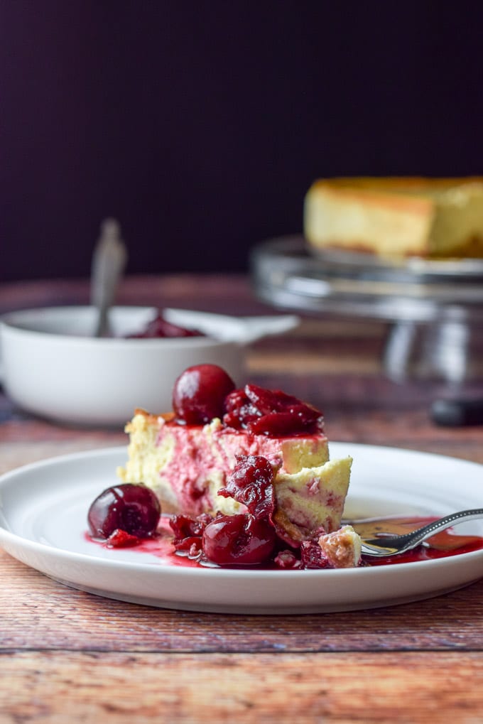 A small plate with the cheesecake covered with cherries and a fork with a bite laying on the plate