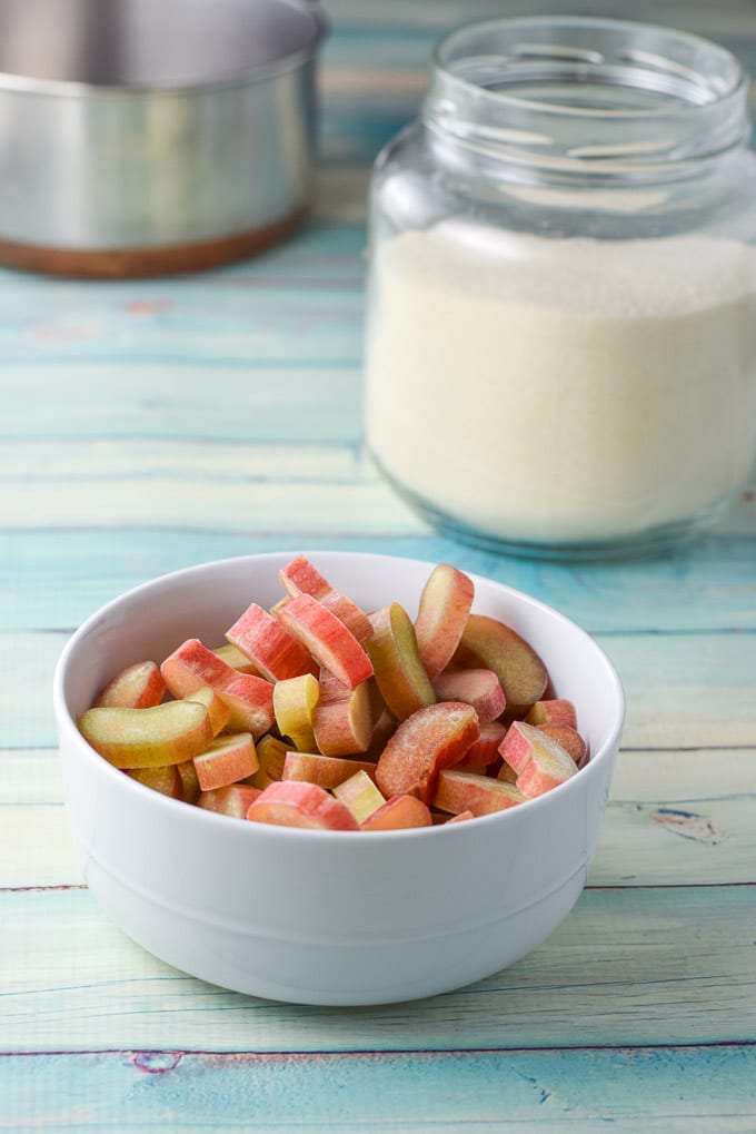 Bowl of cut rhubarb in front, jar of sugar and empty sauce pan in back