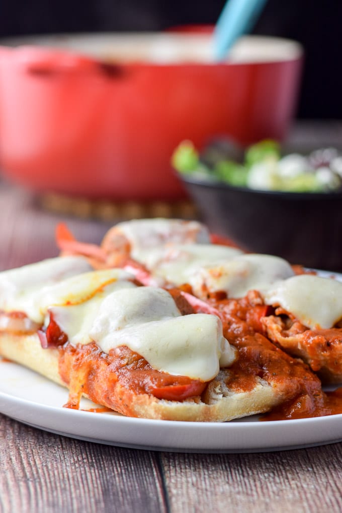 A near vertical view of a white plate with the bread covered with sausage, veggies, gravy and melted cheese
