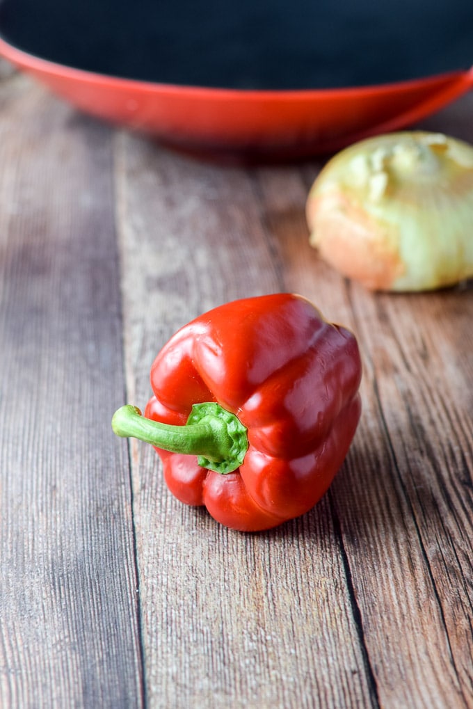 Red bell pepper and onion with a red wok in the background
