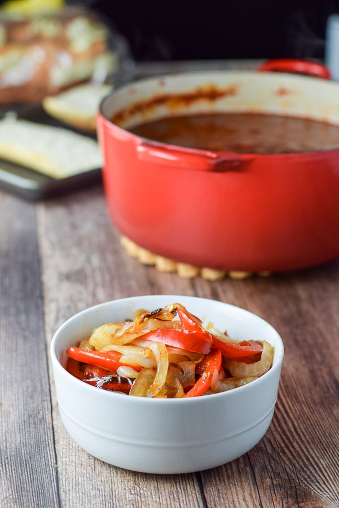 Onion and pepper cooked and in a little bowl. There is a red Dutch oven filled with red gravy in the background