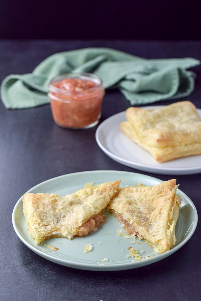 A green plate with a bite taken out of the pastry filled with rhubarb and cream cheese with a white plate in the background with a pastry on it