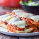 A vertical view of a white plate with the bread covered with sausage, veggies, gravy and melted cheese - square