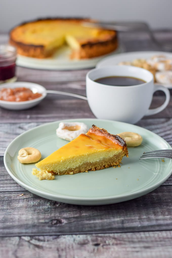 Slice of pie on a green plate with coffee, sauce and the pie in the background