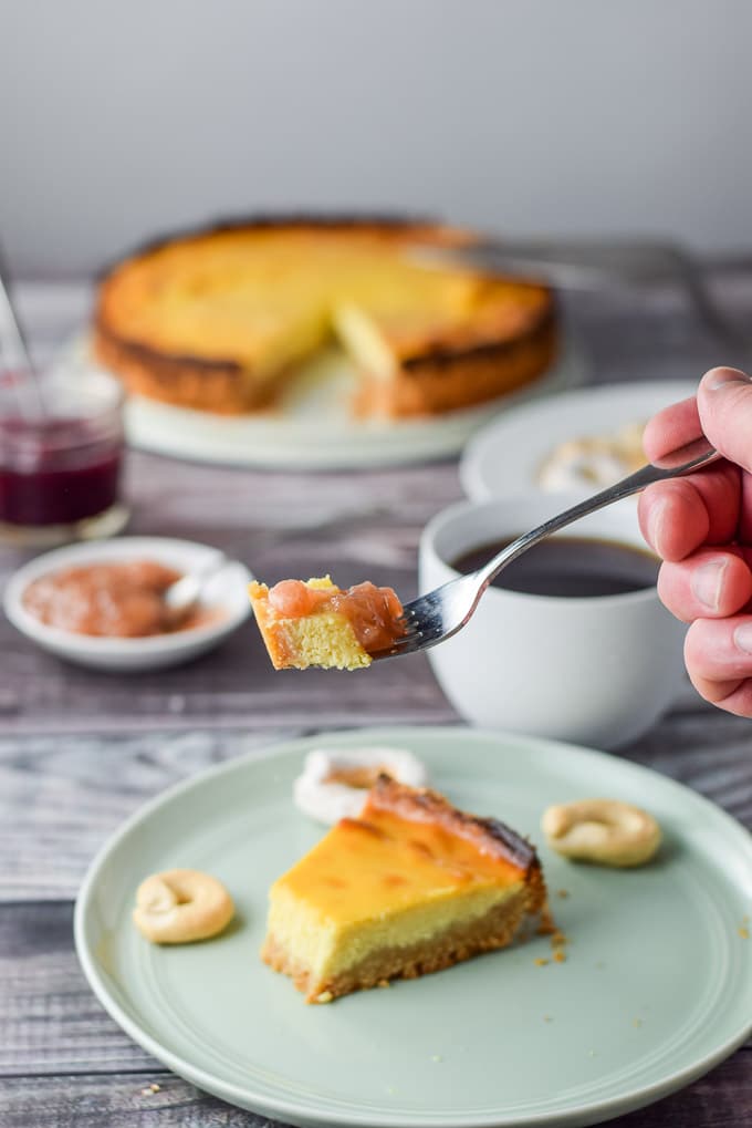 A hand holding a forkful of pie held over the plate with the pie and cookies. There is a coffee, sauce and the rest of the pie in the background