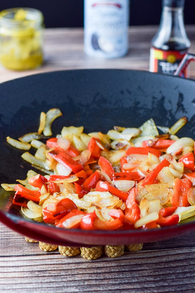 Peppers and onion sautéed for the in a cast iron wok. There is curry, coconut milk and fish sauce in the background