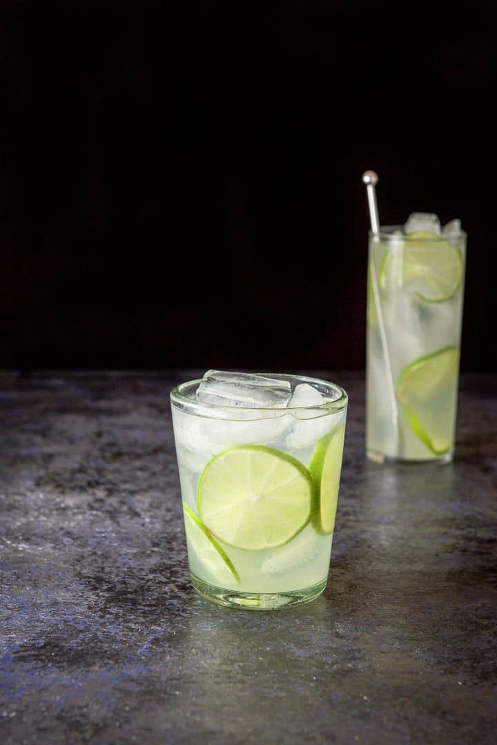 The short glass with three lime wheels in as garnish with the cocktail, also the tall glass in the background