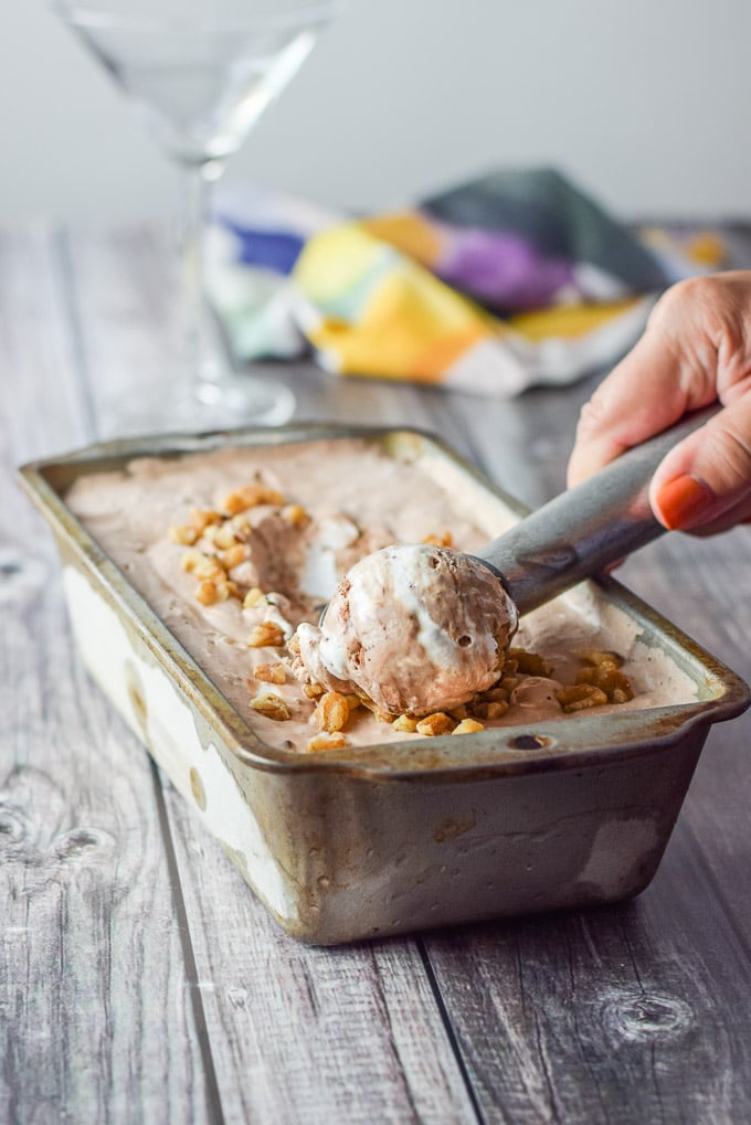 A woman's hand scooping some ice cream out of a bread pan with a martini glass and napkin in the background
